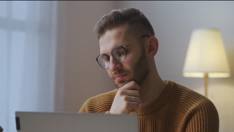 Un-Hombre-Aburrido-Con-Gafas-Está-Escuchando-Y-Mirando-La-Pantalla-Durante-Una-Reunión-En-Línea-Con-Colegas-Sentados-En-Casa-Asintiendo-Con-La-Cabeza,-Retrato-De-Un-Hombre